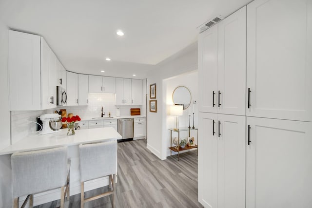 kitchen featuring appliances with stainless steel finishes, light countertops, white cabinetry, and a kitchen breakfast bar