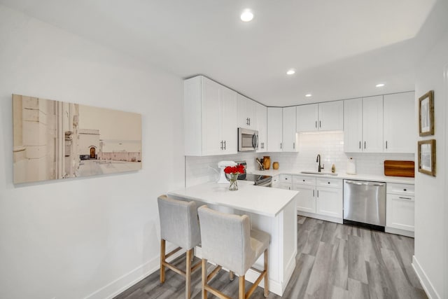 kitchen featuring stainless steel appliances, light countertops, white cabinetry, a peninsula, and a kitchen bar