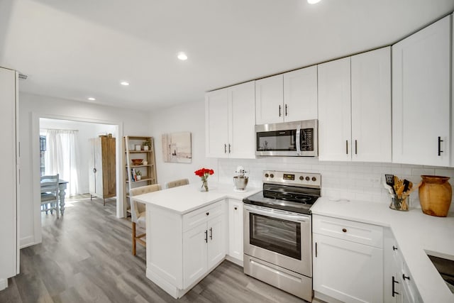 kitchen featuring stainless steel appliances, a peninsula, light countertops, and white cabinetry