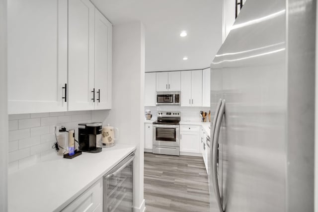 kitchen with beverage cooler, stainless steel appliances, light countertops, and white cabinetry