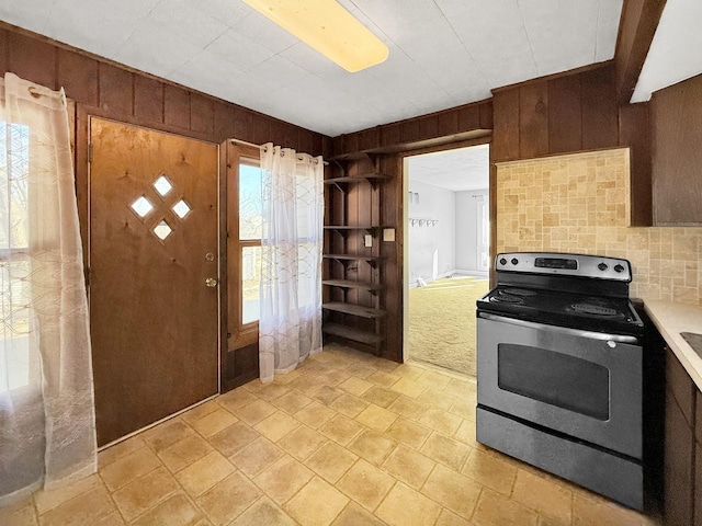 kitchen featuring light countertops, wood walls, decorative backsplash, and stainless steel electric stove