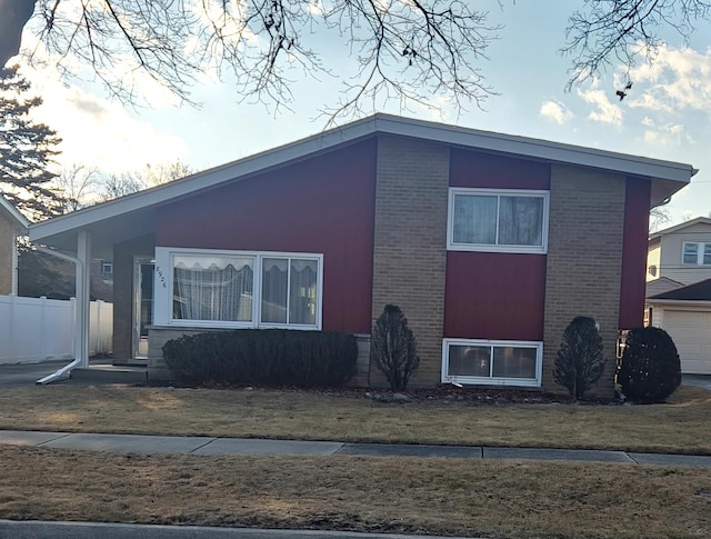 view of side of home featuring a yard, brick siding, and fence