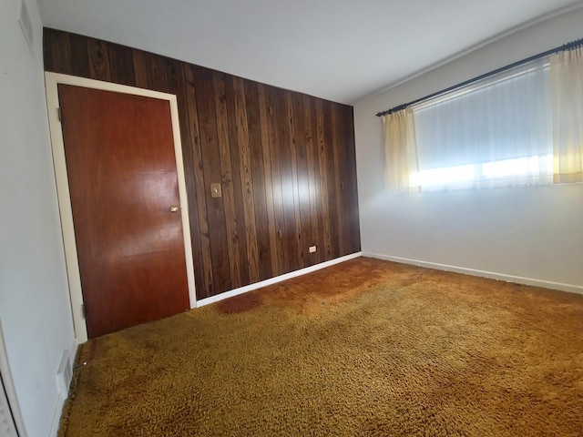 unfurnished room with wood walls, carpet flooring, and baseboards