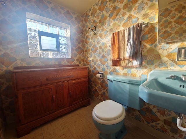 bathroom with toilet, wallpapered walls, and a sink