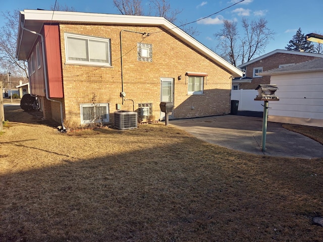 back of house with brick siding, central air condition unit, a lawn, a patio area, and fence