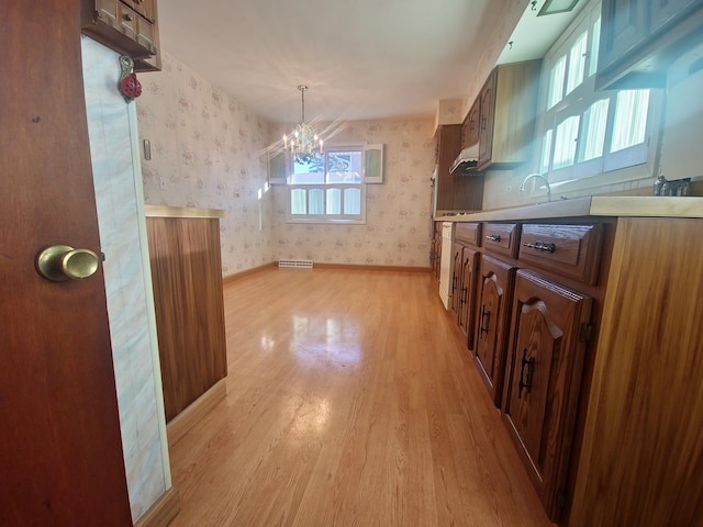 kitchen featuring light wood finished floors, light countertops, an inviting chandelier, baseboards, and wallpapered walls