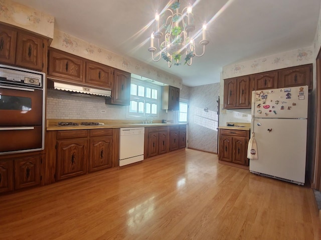 kitchen with white appliances, wallpapered walls, light wood-style floors, premium range hood, and a warming drawer