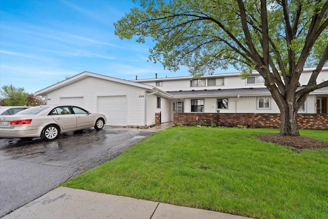 view of front of home featuring an attached garage, brick siding, aphalt driveway, and a front yard