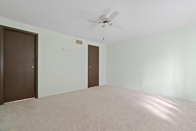 carpeted spare room with visible vents and ceiling fan