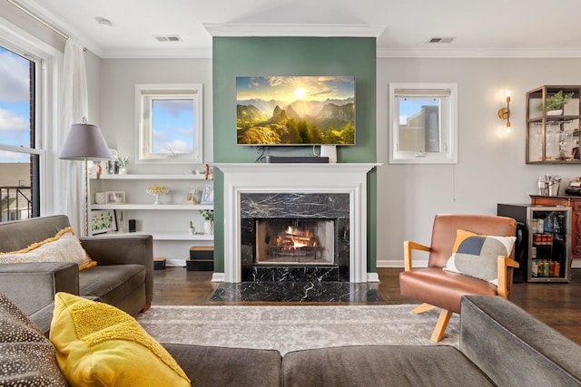 living area featuring ornamental molding, visible vents, a fireplace, and wood finished floors