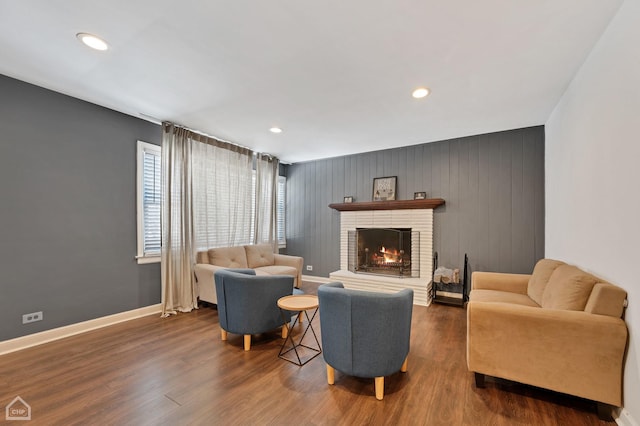 living area with dark wood-type flooring, recessed lighting, a brick fireplace, and baseboards