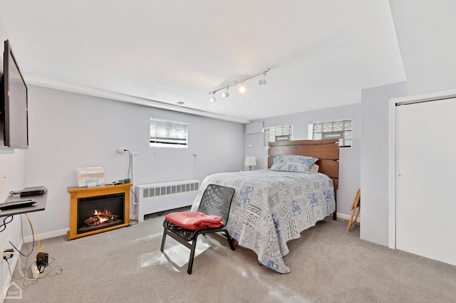 bedroom with baseboards, radiator heating unit, a glass covered fireplace, and light colored carpet