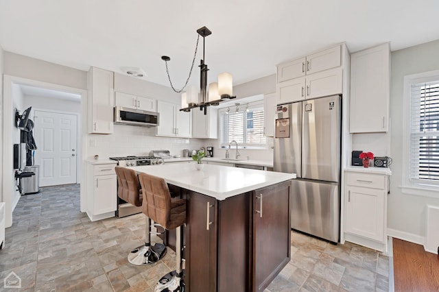 kitchen with appliances with stainless steel finishes, a center island, white cabinets, and light countertops