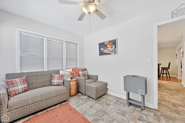 living area featuring stone finish flooring, ceiling fan, and baseboards