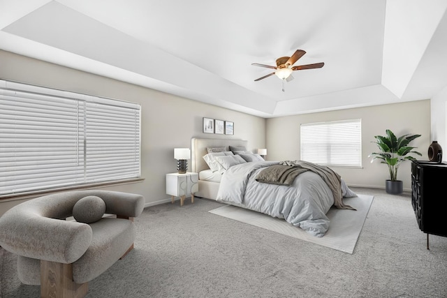 carpeted bedroom with ceiling fan, a raised ceiling, and baseboards