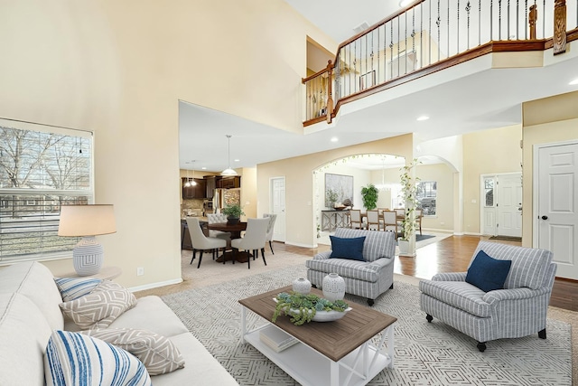 living area with wood finished floors, recessed lighting, arched walkways, baseboards, and a towering ceiling