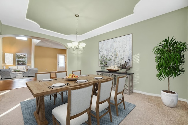 dining area featuring baseboards, light colored carpet, a tray ceiling, an inviting chandelier, and arched walkways