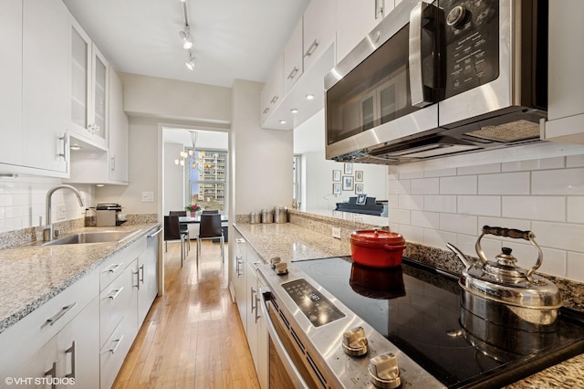 kitchen with light stone countertops, light wood finished floors, appliances with stainless steel finishes, and a sink