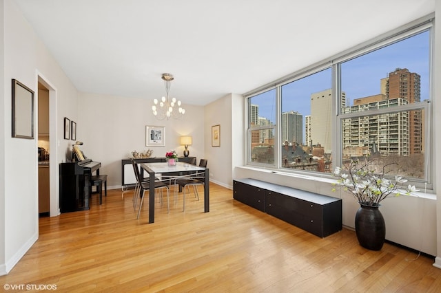 dining area with baseboards, an inviting chandelier, light wood-style flooring, and a city view