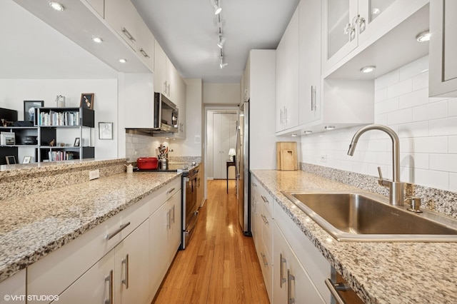 kitchen featuring stainless steel appliances, tasteful backsplash, white cabinets, a sink, and light wood-type flooring