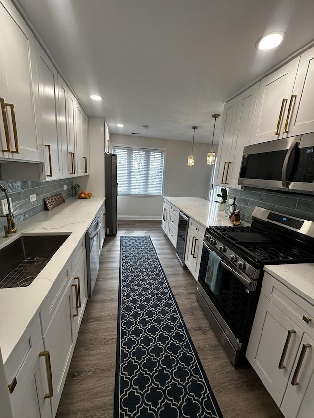 kitchen with appliances with stainless steel finishes, dark wood finished floors, a sink, and backsplash