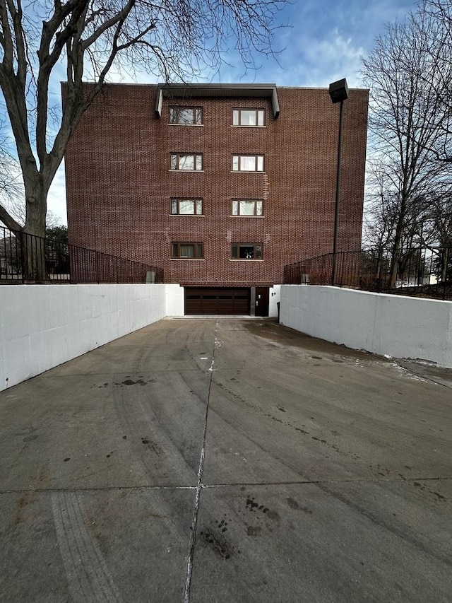 view of building exterior with concrete driveway, an attached garage, and fence