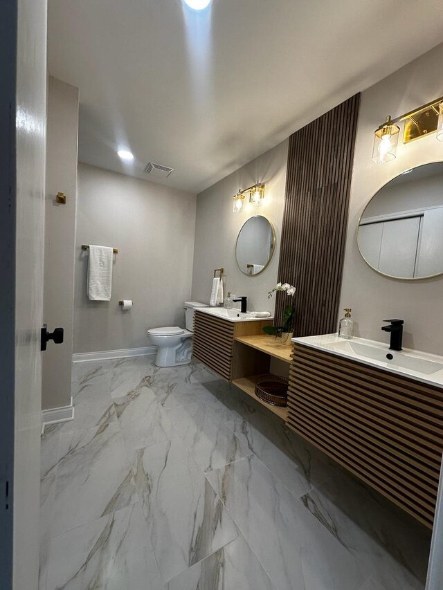 bathroom featuring visible vents, toilet, a sink, marble finish floor, and two vanities