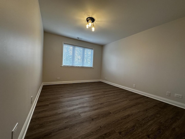 unfurnished room featuring dark wood finished floors, visible vents, and baseboards