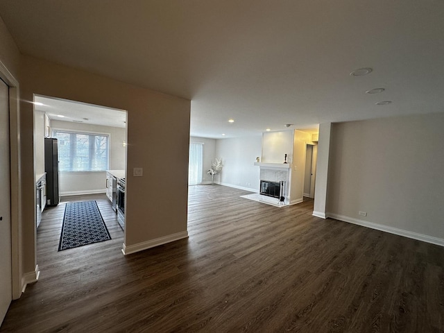 unfurnished living room with a fireplace with flush hearth, recessed lighting, dark wood-type flooring, and baseboards