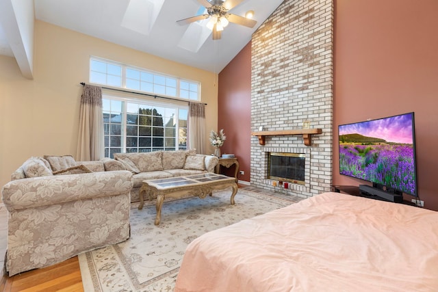 bedroom with high vaulted ceiling, a fireplace, a skylight, a ceiling fan, and light wood finished floors