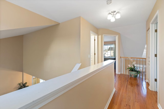 corridor featuring baseboards, light wood finished floors, and an upstairs landing