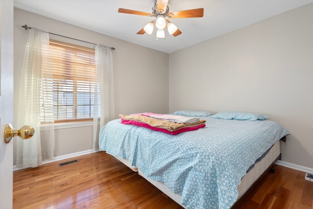 bedroom with ceiling fan, wood finished floors, visible vents, and baseboards