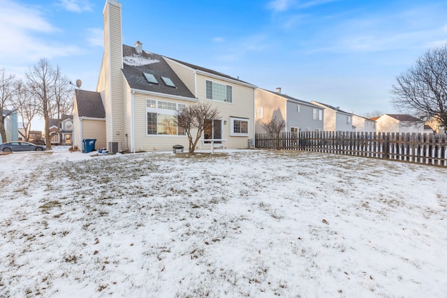 snow covered rear of property with a residential view, central AC, fence, and a chimney