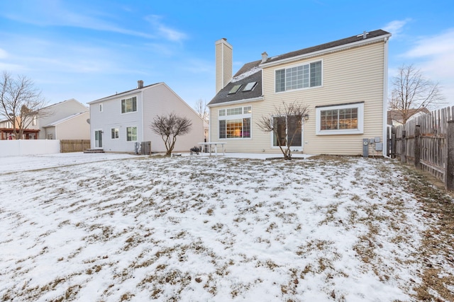 snow covered rear of property featuring a chimney, fence, and central air condition unit