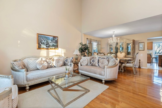 living room featuring a notable chandelier, a towering ceiling, baseboards, and wood finished floors