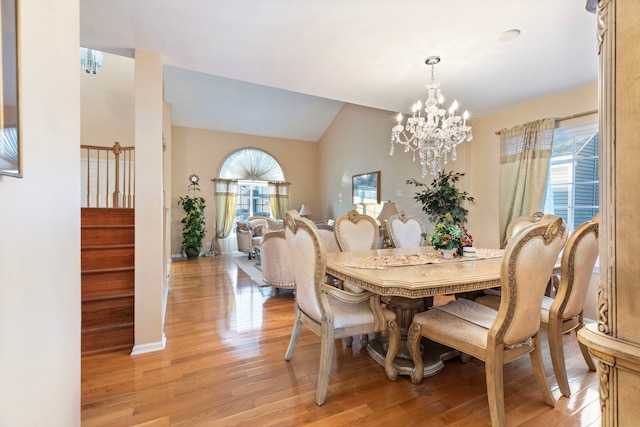 dining area with an inviting chandelier, light wood-style flooring, stairs, and vaulted ceiling