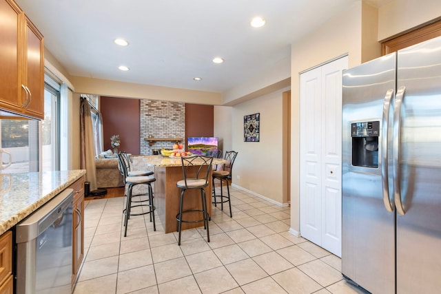 kitchen featuring appliances with stainless steel finishes, brown cabinets, light stone counters, and a kitchen bar