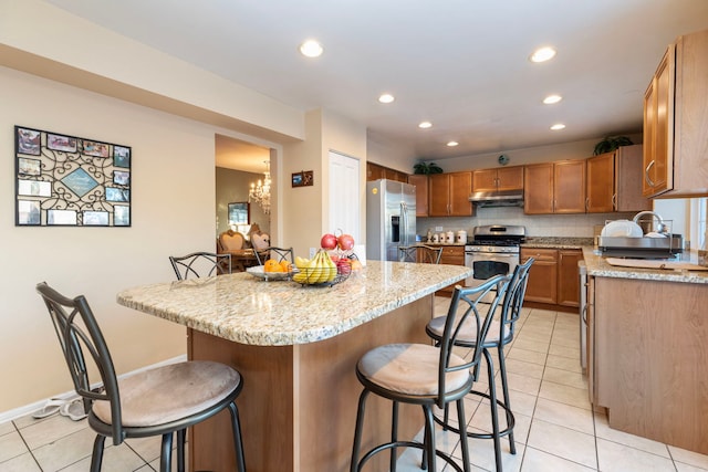 kitchen with light stone countertops, under cabinet range hood, a breakfast bar area, and stainless steel appliances