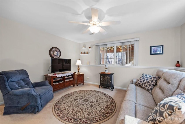 living room featuring a wood stove, light carpet, ceiling fan, and baseboards