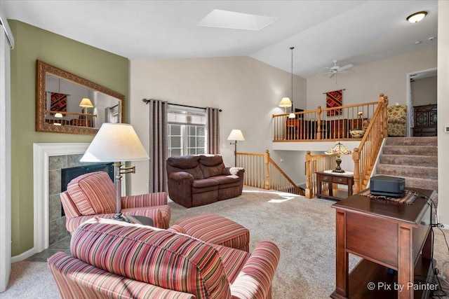 carpeted living area with lofted ceiling with skylight, ceiling fan, a fireplace, and stairway