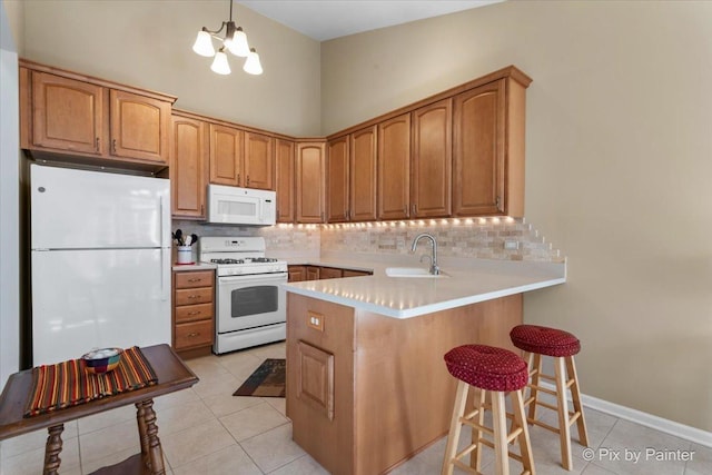 kitchen featuring decorative backsplash, a sink, white appliances, a peninsula, and a kitchen bar