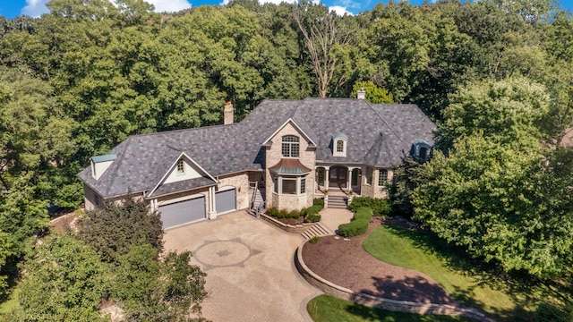 view of front facade with stone siding, a forest view, driveway, and a chimney