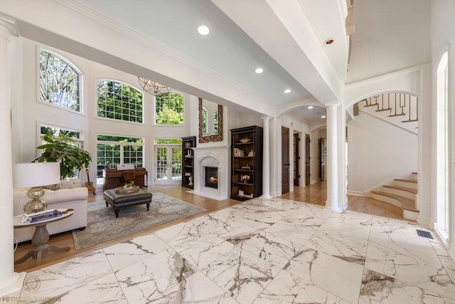 living room with ornate columns, a high ceiling, a fireplace with flush hearth, arched walkways, and ornamental molding