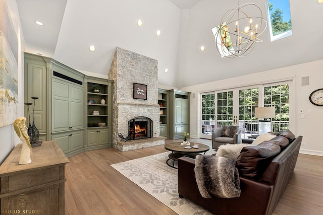 living area featuring baseboards, high vaulted ceiling, light wood-style flooring, a stone fireplace, and a chandelier