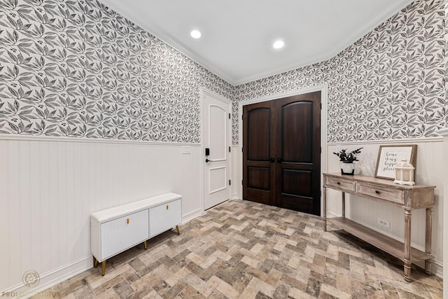 foyer entrance featuring wallpapered walls, a wainscoted wall, ornamental molding, recessed lighting, and brick floor