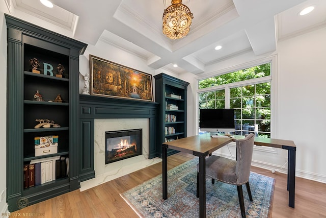 office area with built in features, coffered ceiling, crown molding, light wood finished floors, and a premium fireplace