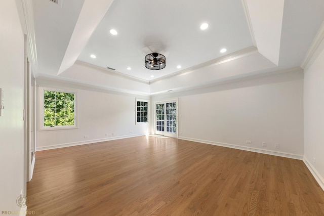 spare room with light wood-type flooring, a raised ceiling, and ornamental molding