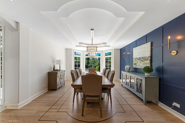 dining area with light wood finished floors, a decorative wall, baseboards, a tray ceiling, and a notable chandelier