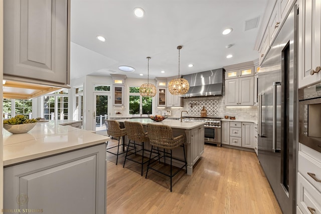 kitchen featuring high end appliances, decorative backsplash, a kitchen bar, wall chimney range hood, and light wood-type flooring