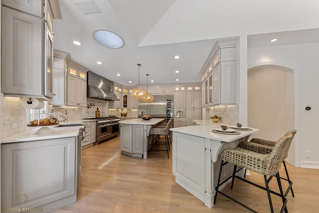 kitchen with a breakfast bar area, high end appliances, a sink, light wood-style floors, and wall chimney exhaust hood